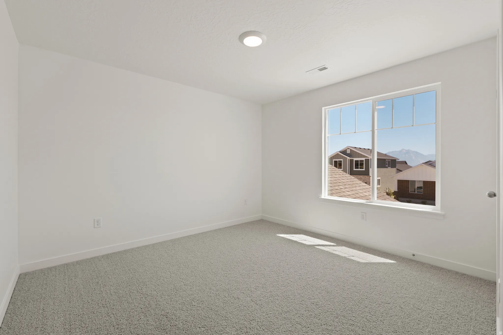 Bright interior room featuring a large window, light gray carpeting, crisp white walls, and a recessed ceiling light