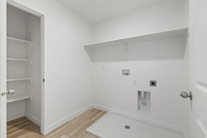 Dedicated laundry room featuring wood-finish flooring, a built-in utility sink base, and overhead shelving