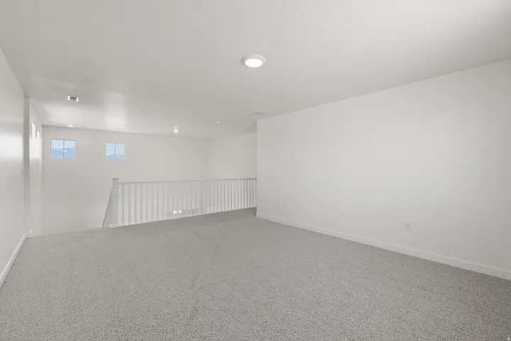 Spacious loft area featuring light gray carpet flooring and white painted walls