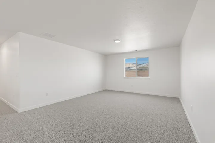 Spacious room featuring light gray carpeting, white painted walls, and a large window showcasing a mountainous landscape