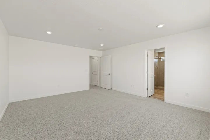 Spacious room featuring light gray carpeting, crisp white walls, and recessed lighting