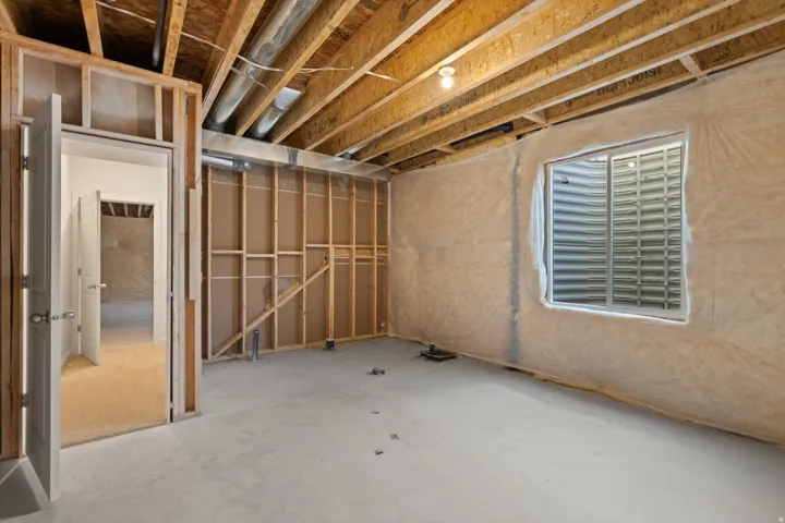 Unfinished basement space with exposed wood framing, an egress window, and concrete flooring