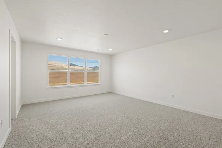 Spacious room featuring light gray carpeting, crisp white walls, recessed ceiling lighting, and a multi-pane window showcasing a scenic natural landscape