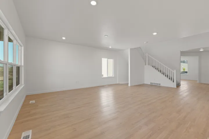 Spacious room featuring wood-finish flooring, ample natural light from multiple windows, recessed lighting, and a white staircase with balusters