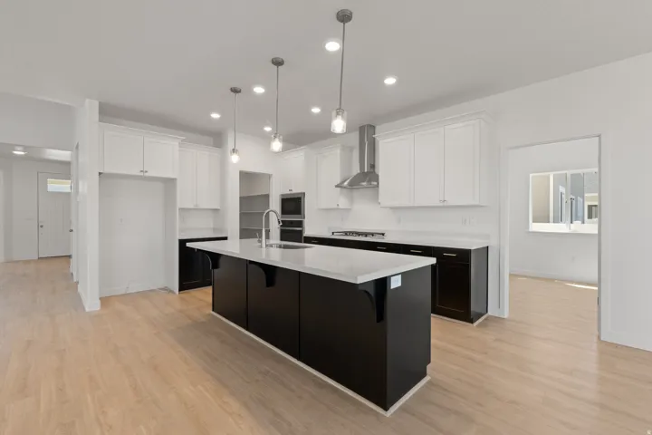 Modern kitchen featuring a large central island with a sink, stainless steel appliances, white upper cabinetry, dark lower cabinetry, and wood-finish flooring