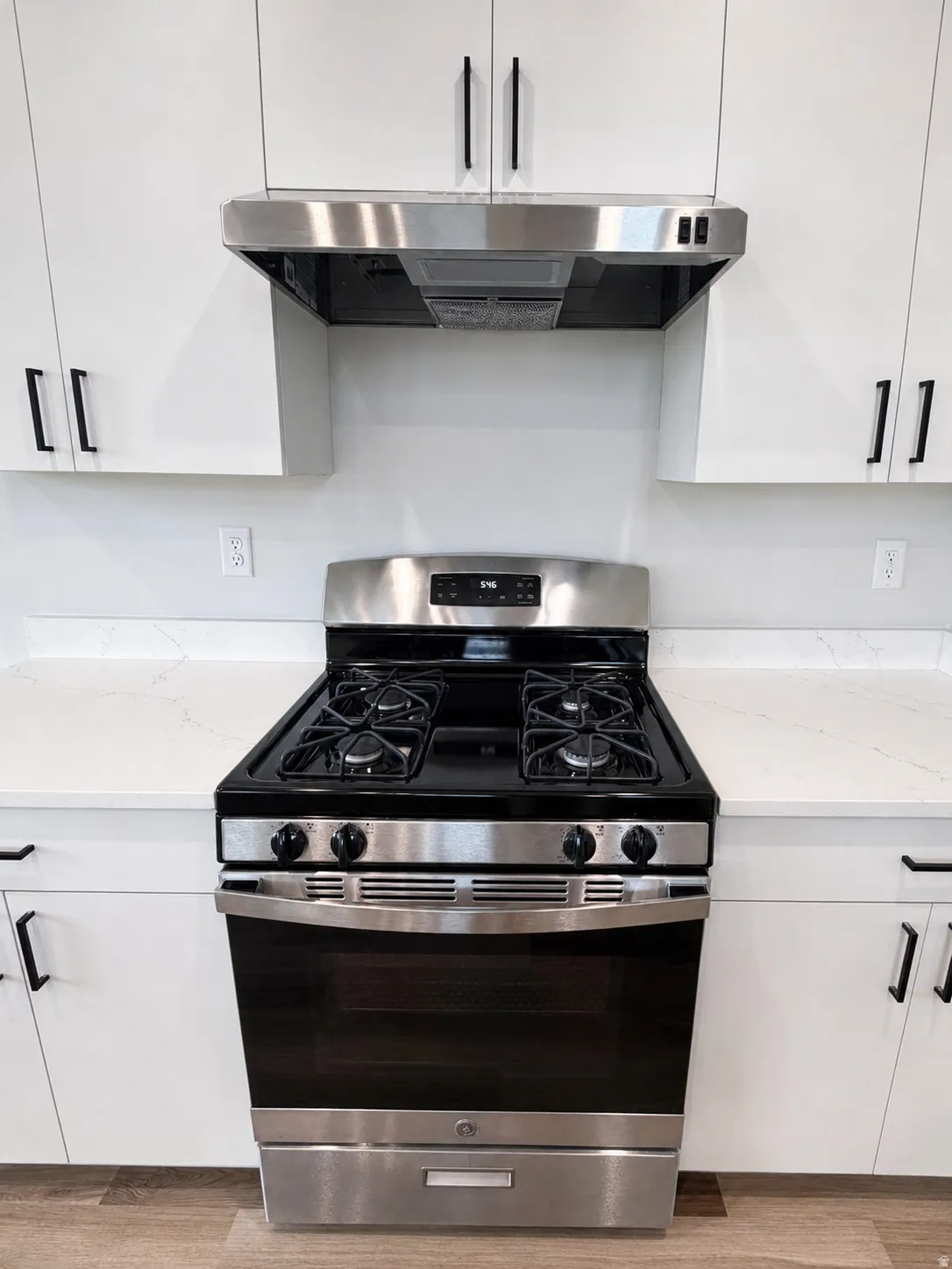 Kitchen featuring a stainless steel range with a gas cooktop, a coordinating stainless steel range hood, crisp white cabinetry with matte black hardware, and bright white countertops