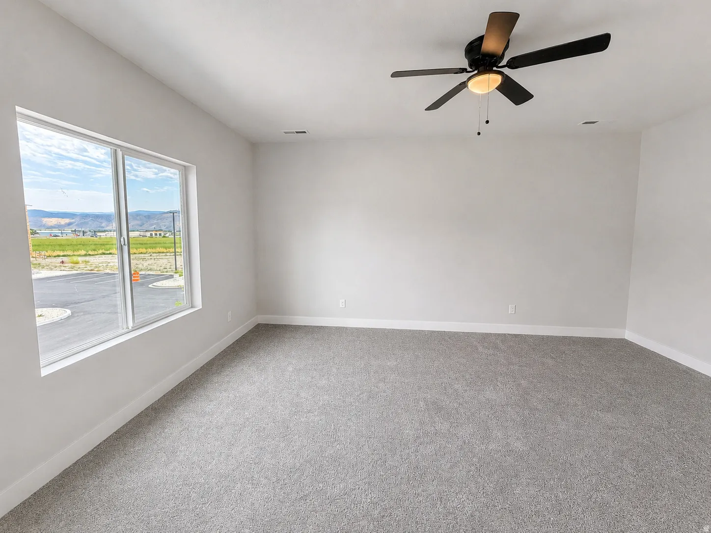 Spacious interior featuring a large window, gray carpet flooring, white baseboards, and a ceiling fan with integrated lighting