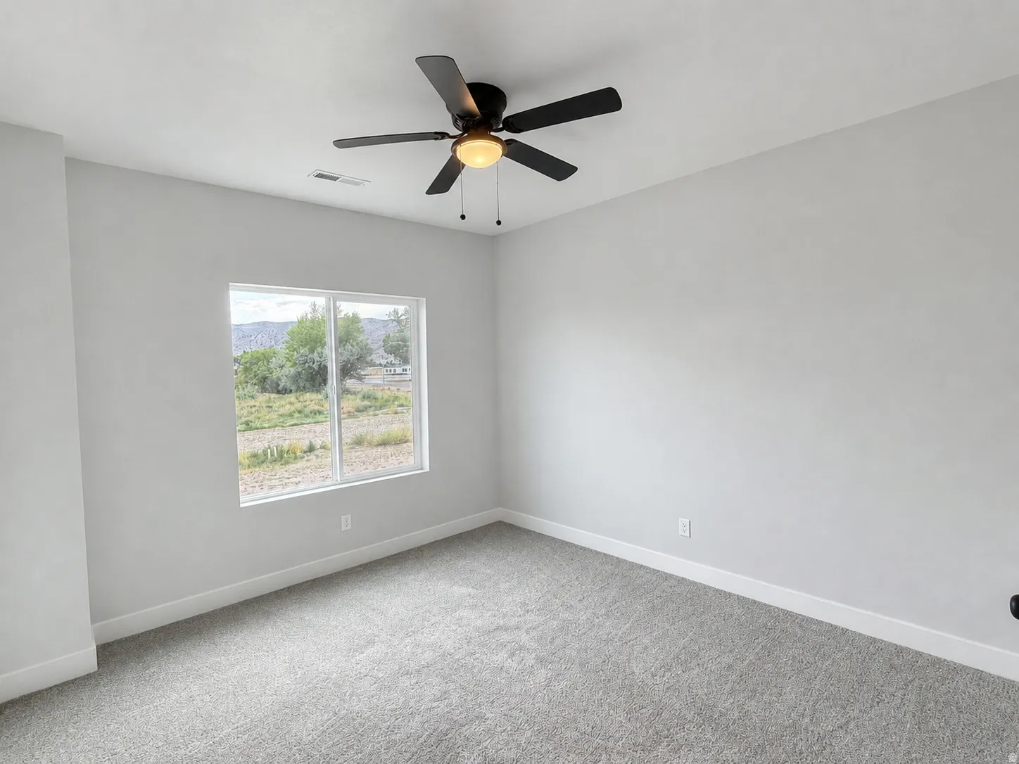 Bright room featuring a large window, dark ceiling fan with integrated lighting, light gray carpet, white baseboards, and neutral wall tones