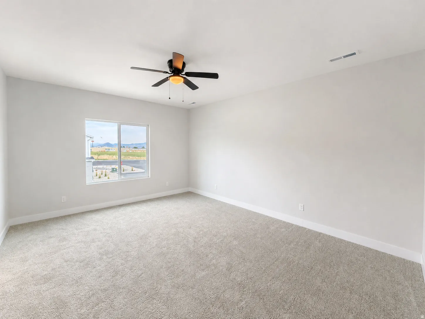 Bright interior space with light gray carpet, white baseboards, and a window offering a distant landscape