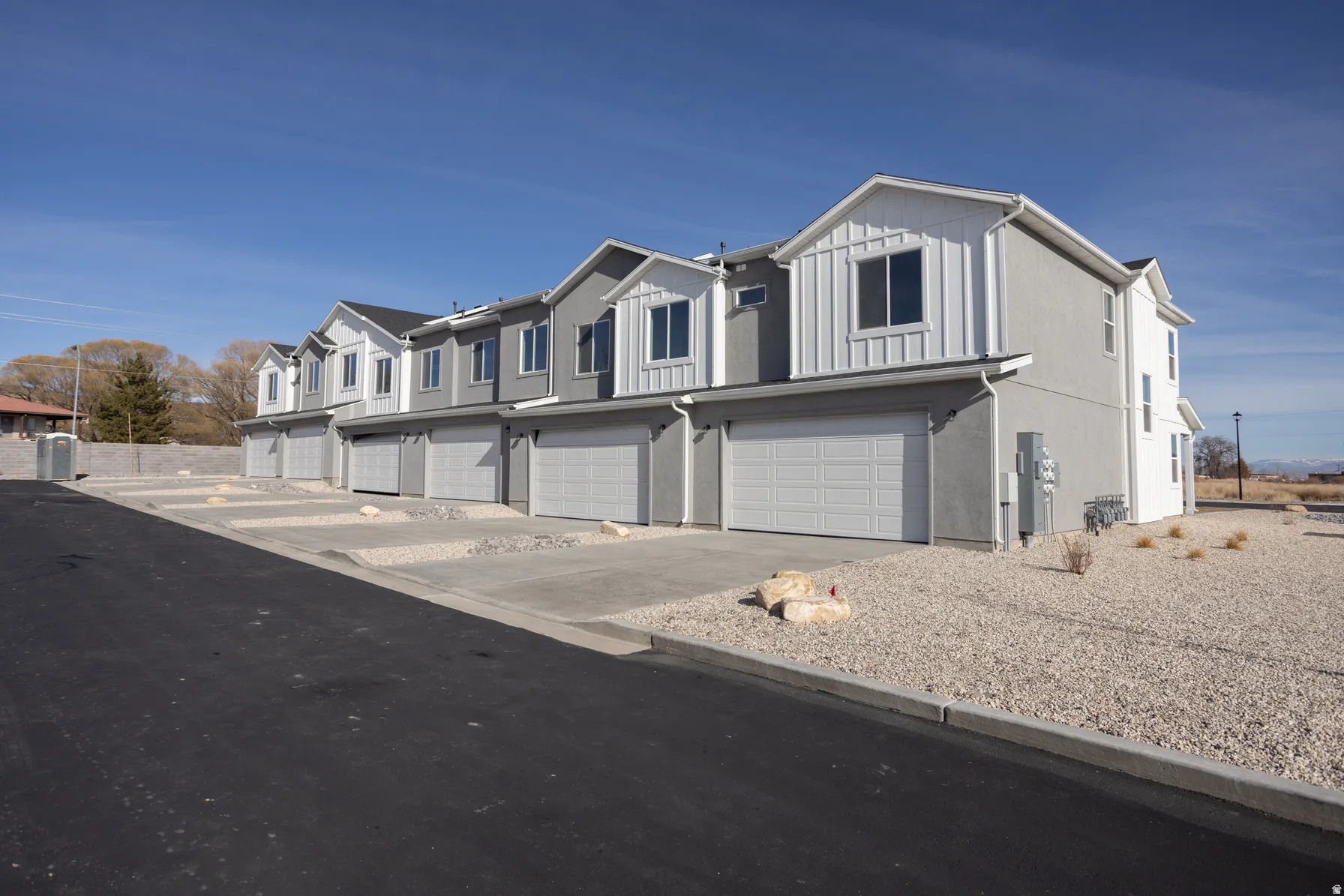 Modern townhome exteriors featuring stucco and vertical siding, attached garages, gravel landscaping, and paved driveways