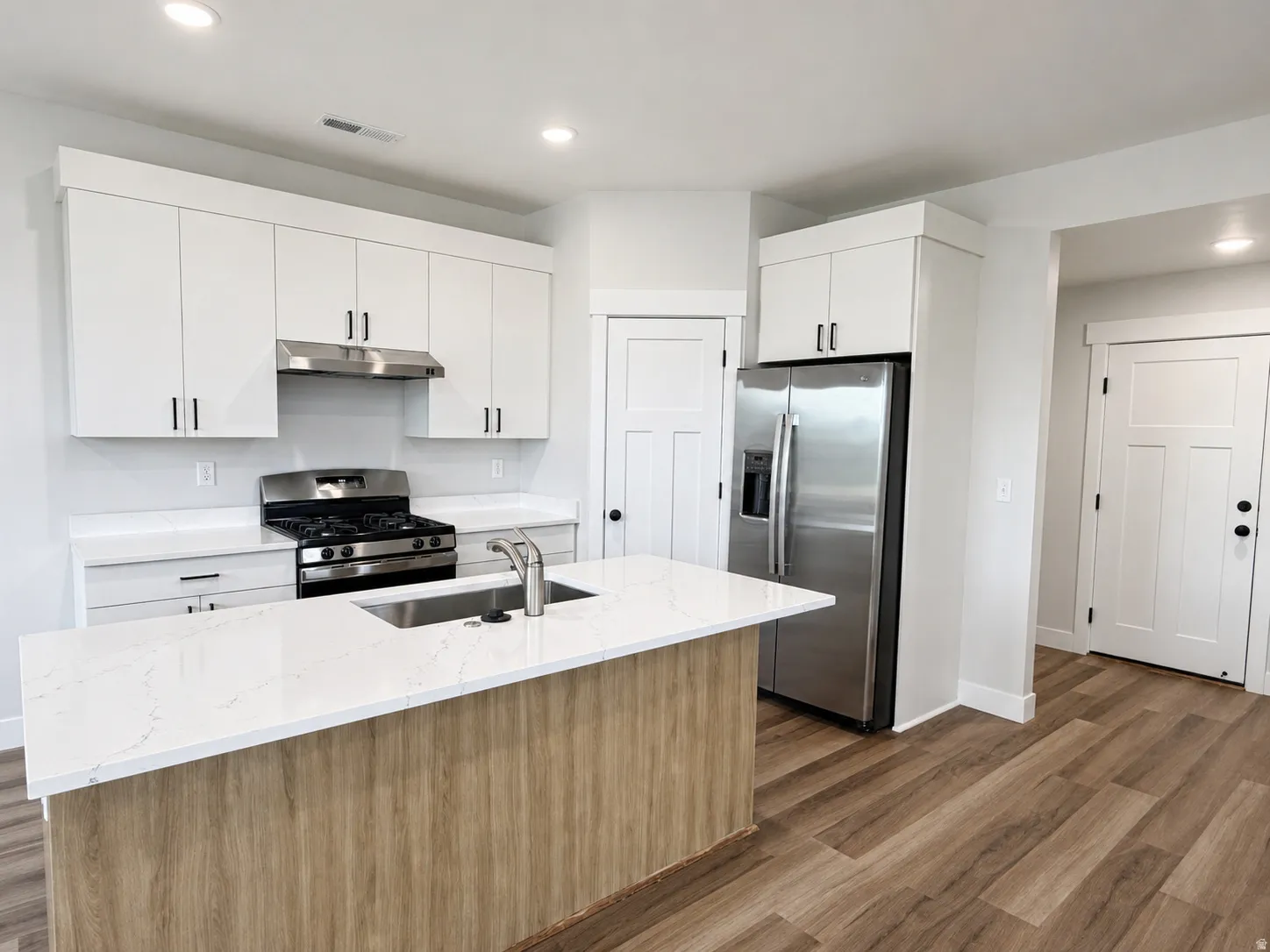 Modern kitchen featuring a central island with an integrated sink, white quartz countertops, stainless steel appliances, and wood-finish flooring