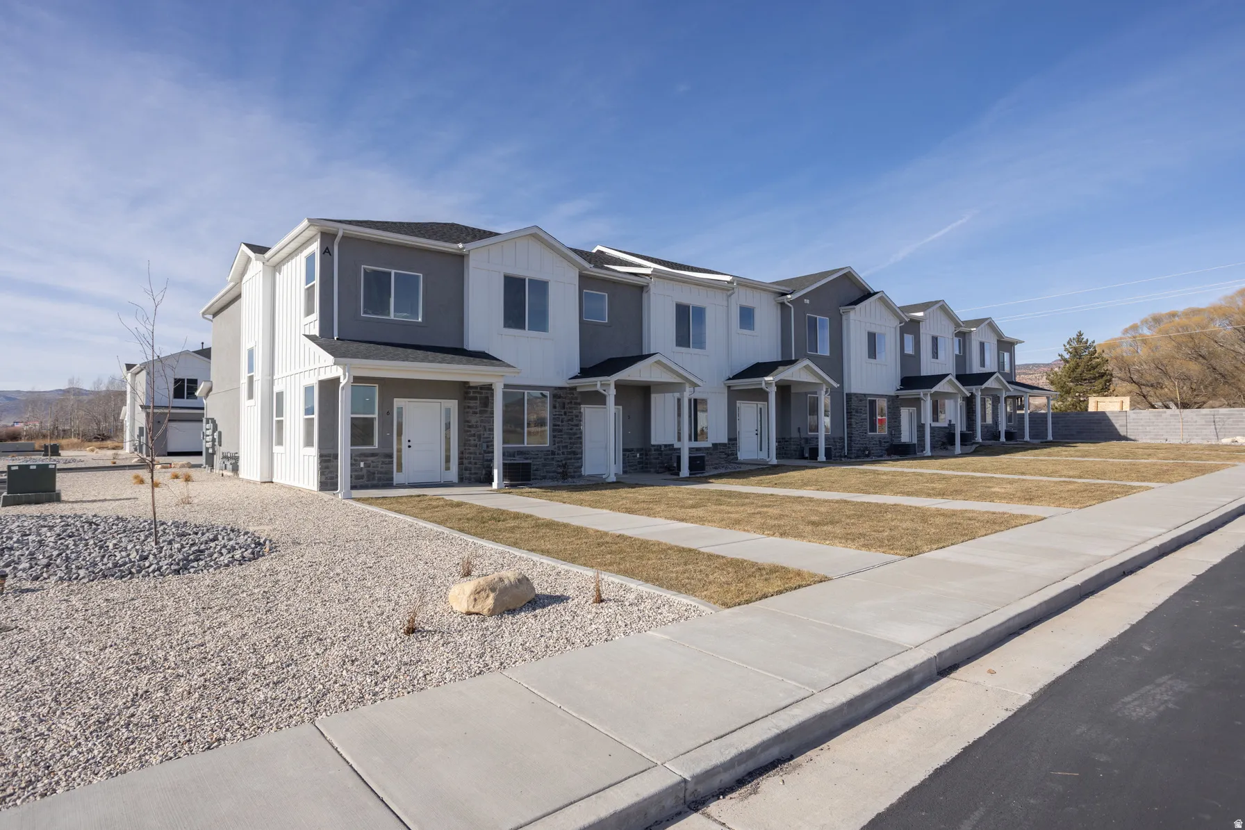 Contemporary townhome facades featuring a mix of white vertical siding, gray horizontal siding, and stone veneer accents