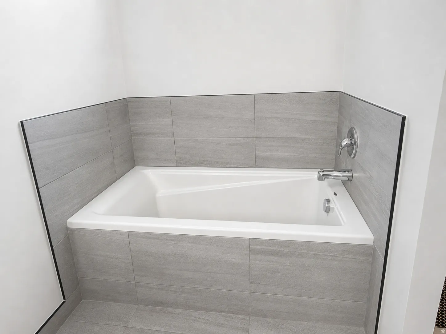 Built-in bathtub with a white finish, surrounded by large format gray tile walls and matching tile flooring