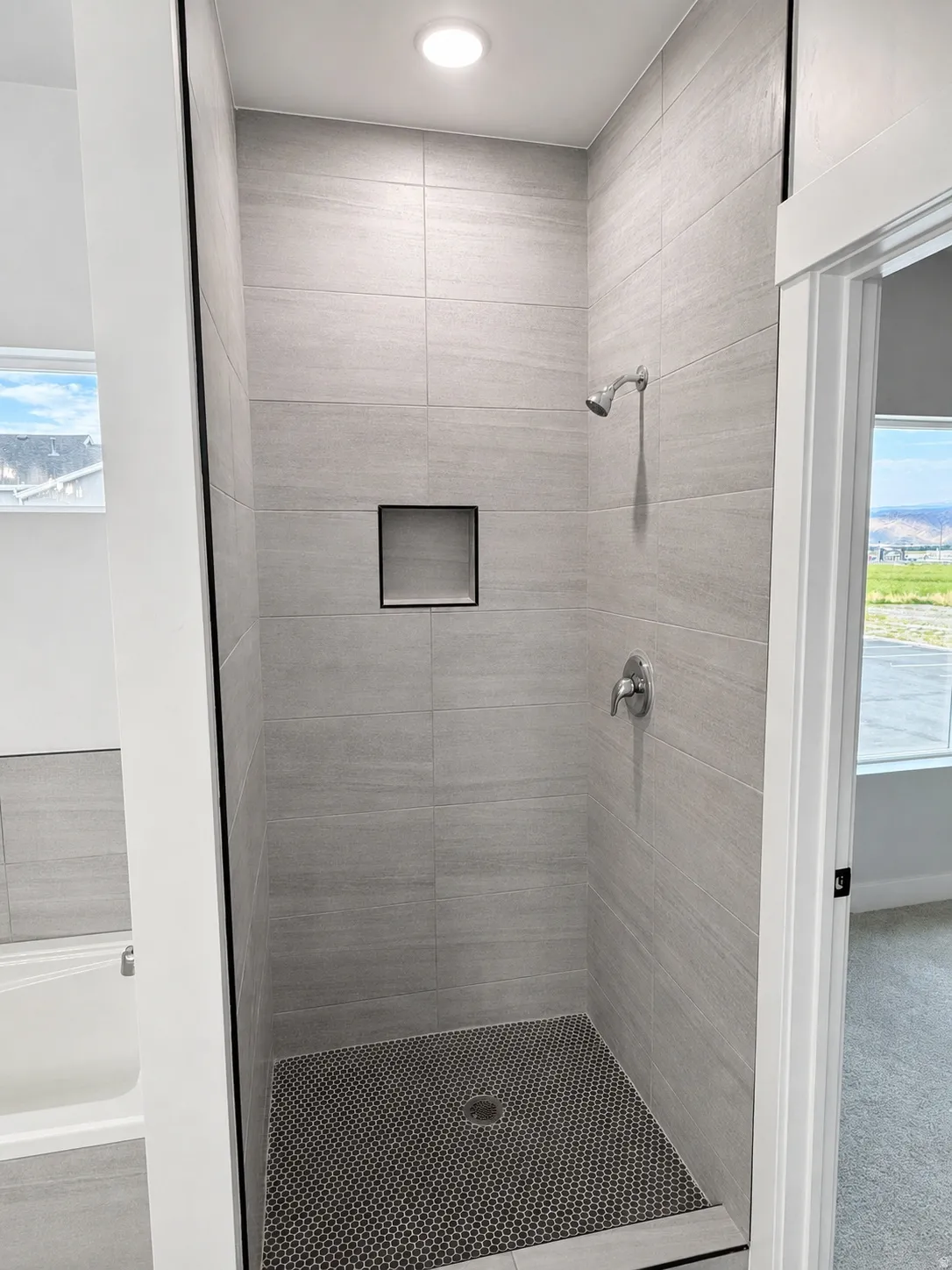 Walk-in shower featuring light gray large format tile walls and a dark penny tile floor