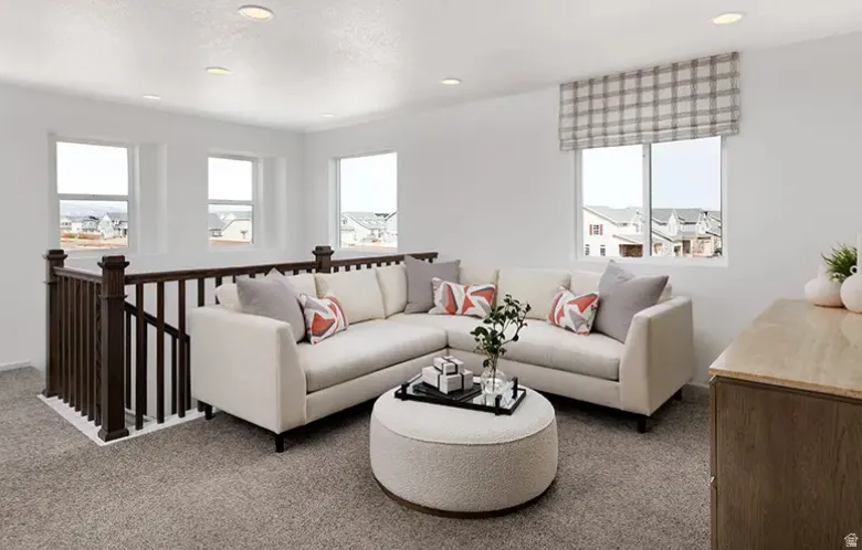 Carpeted loft area featuring a dark wood railing, white walls, and recessed lighting