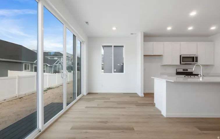 Open-concept living space with wood-finish flooring, white cabinetry, a kitchen island with a sink, and stainless steel appliances