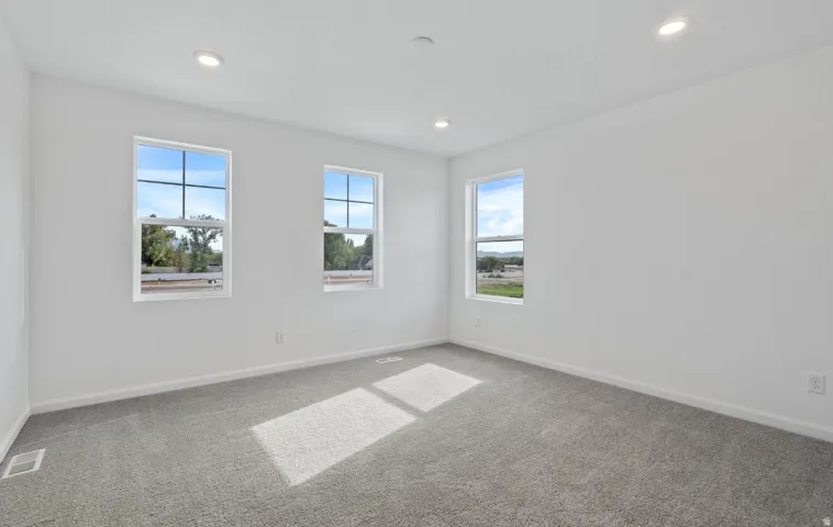 Light gray carpeting, white walls, three windows with white trim, and recessed lighting