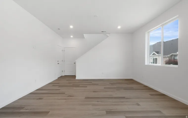 Recessed lighting, wood-finish flooring, white walls, and a large window