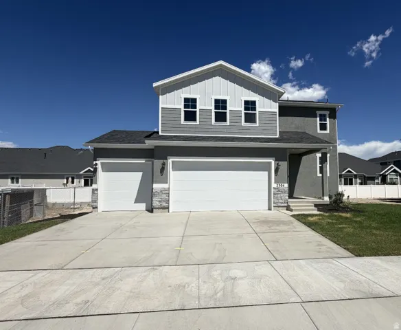 Two-story residence featuring a two-car garage, gray siding, stone accents, and a concrete driveway