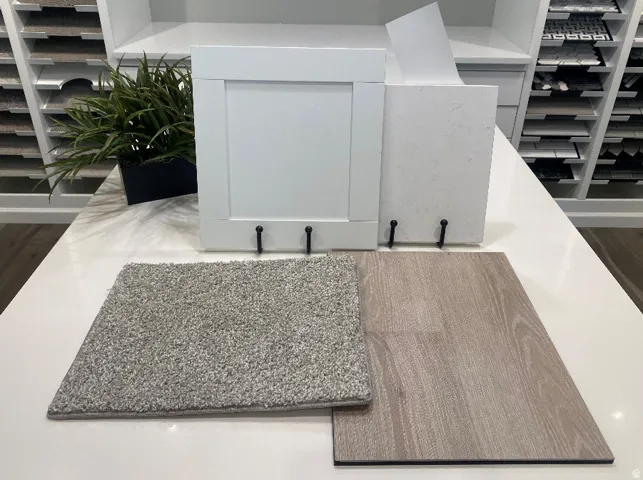 Contemporary material selection featuring a white shaker cabinet door, light-toned wood-finish flooring, a light gray carpet sample, and a white countertop sample