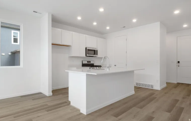 White cabinetry, stainless steel appliances, recessed lighting, wood-finish flooring, and a central island with an integrated sink