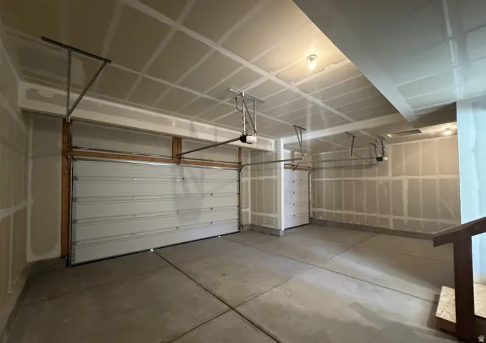 Spacious garage with two overhead doors, concrete flooring, and exposed ceiling joists