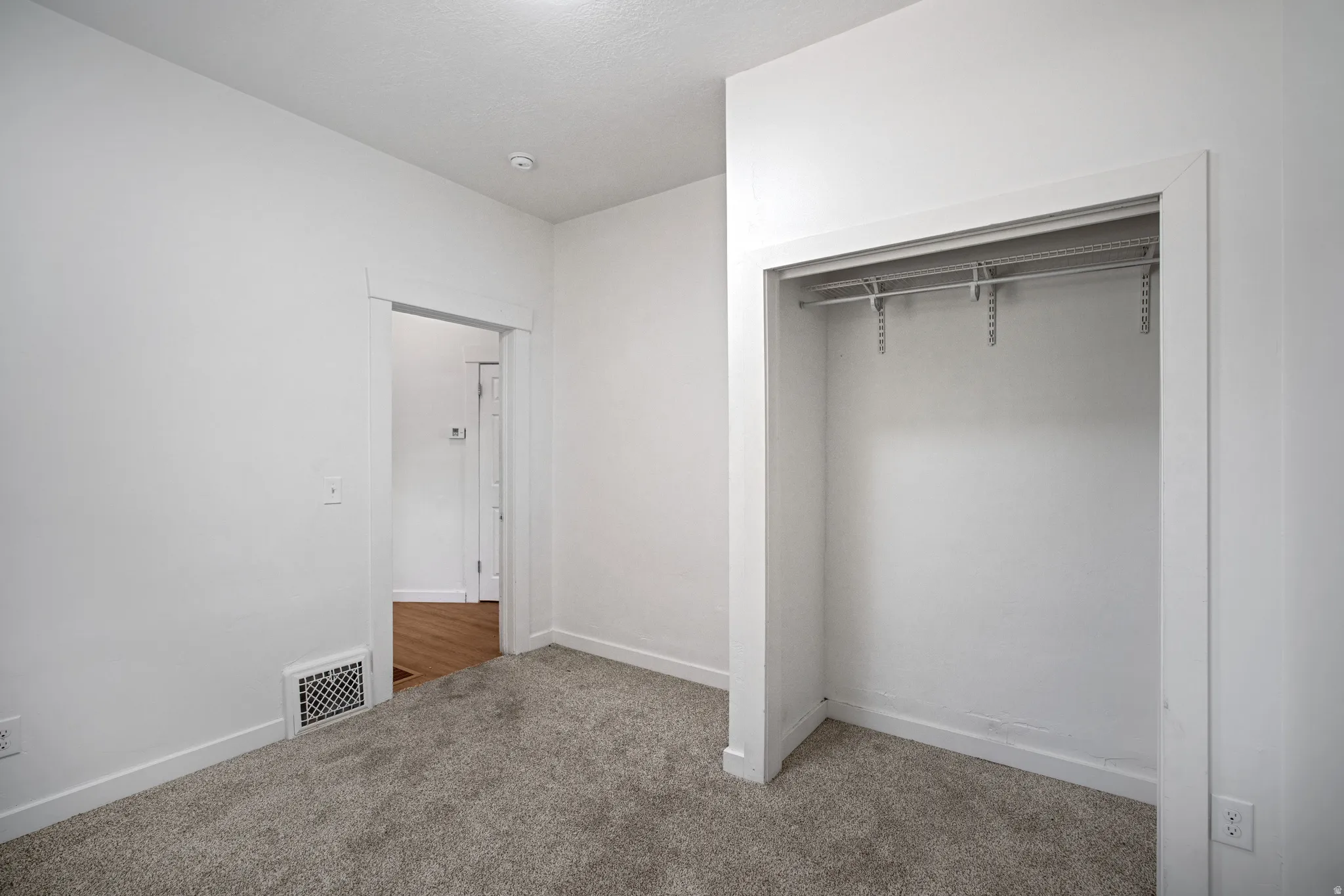 Room featuring light gray carpeting, crisp white walls, a built-in closet with adjustable shelving and hanging rods, and a white baseboard trim