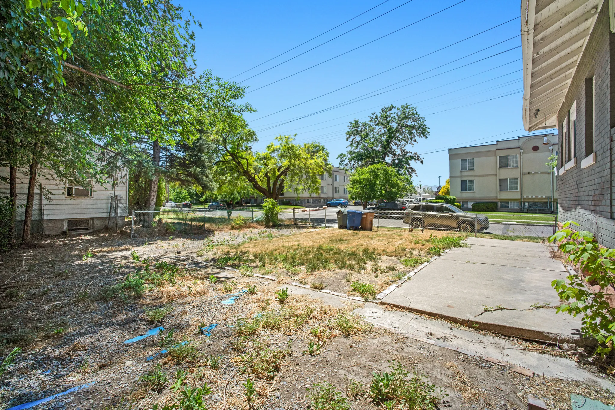 Spacious property exterior featuring a concrete walkway, mature trees, and an expansive undeveloped yard space