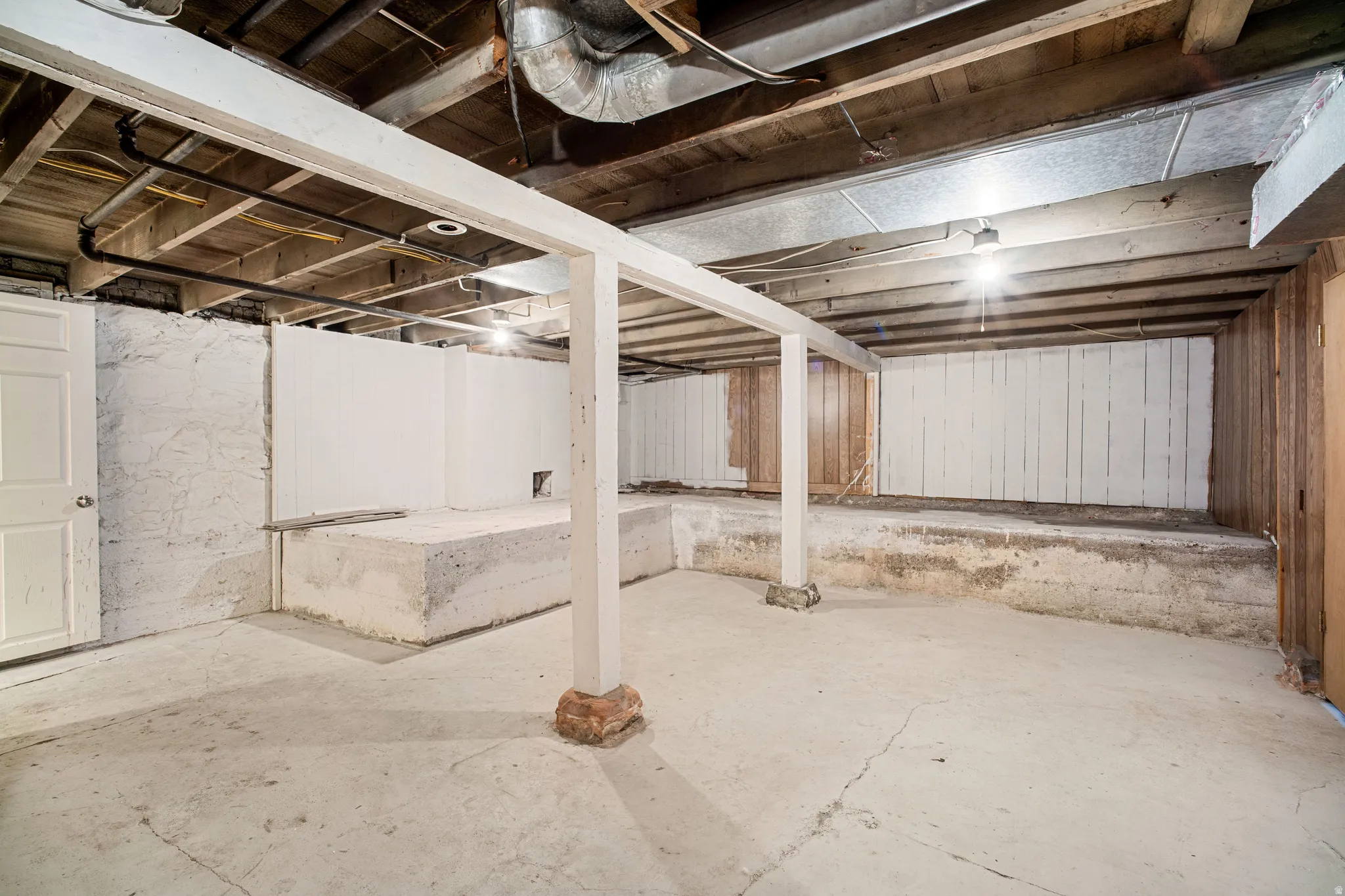 Unfinished basement with concrete flooring and exposed wooden ceiling joists