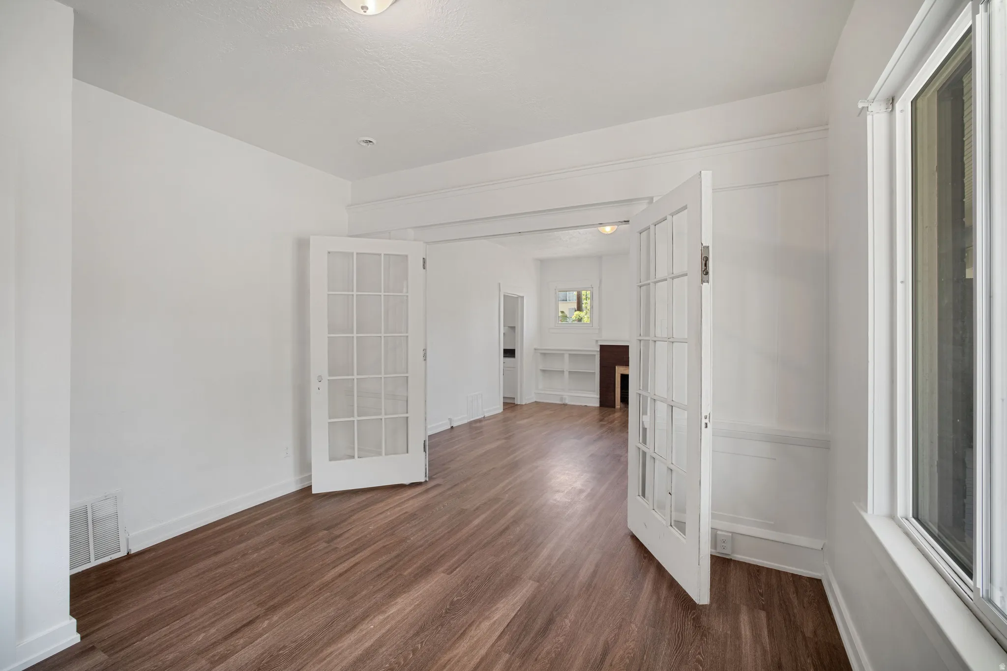 Room featuring wood-finish flooring, white walls, and a large window providing natural light