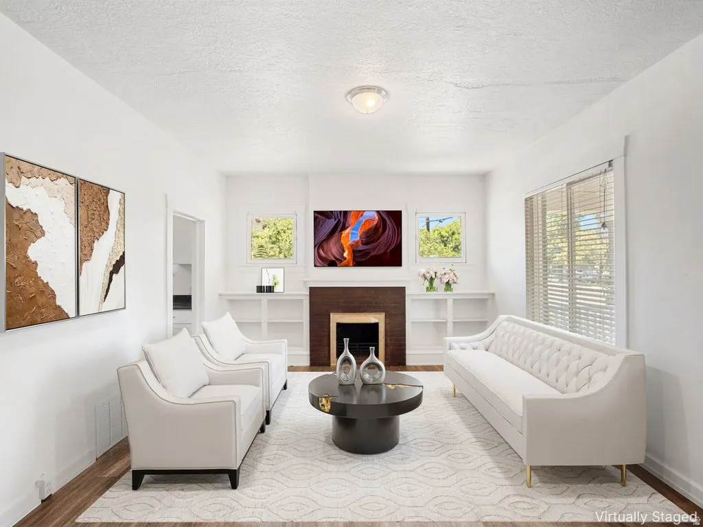 Bright living area featuring wood-finish flooring, a decorative fireplace with a dark wood mantel, built-in shelving, white walls, and a recessed ceiling light fixture