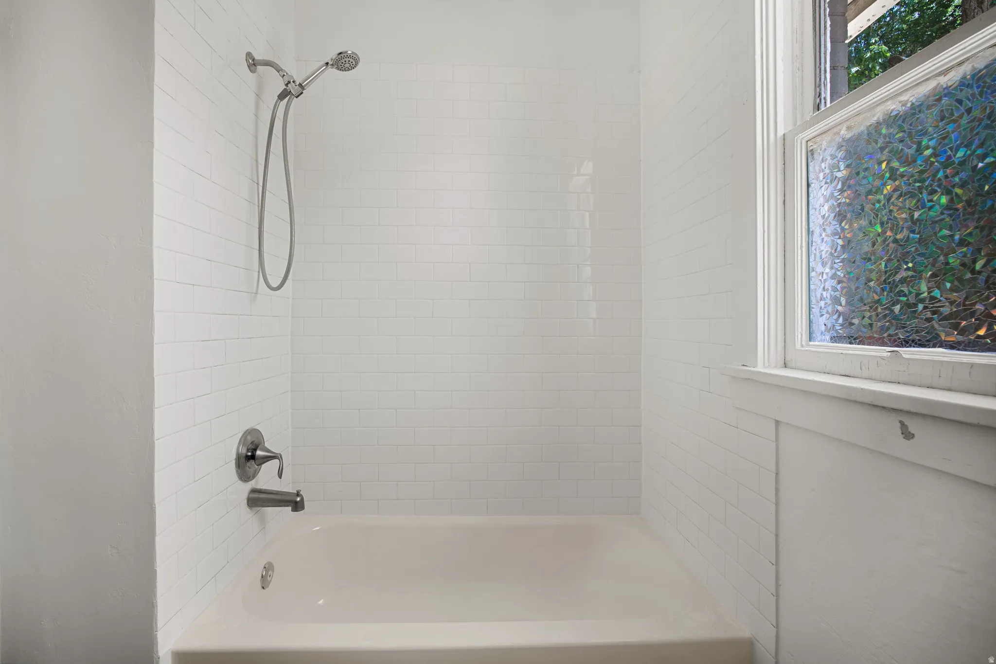 Bathtub with white subway tile surround, polished chrome fixtures, and a decorative privacy window