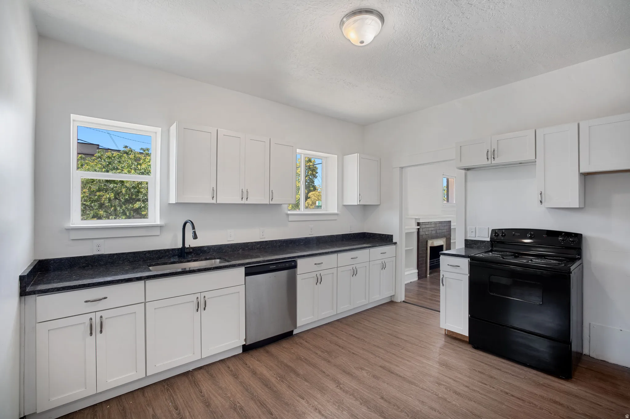 Modern kitchen featuring wood-finish flooring, white cabinetry, dark countertops, and a stainless steel dishwasher