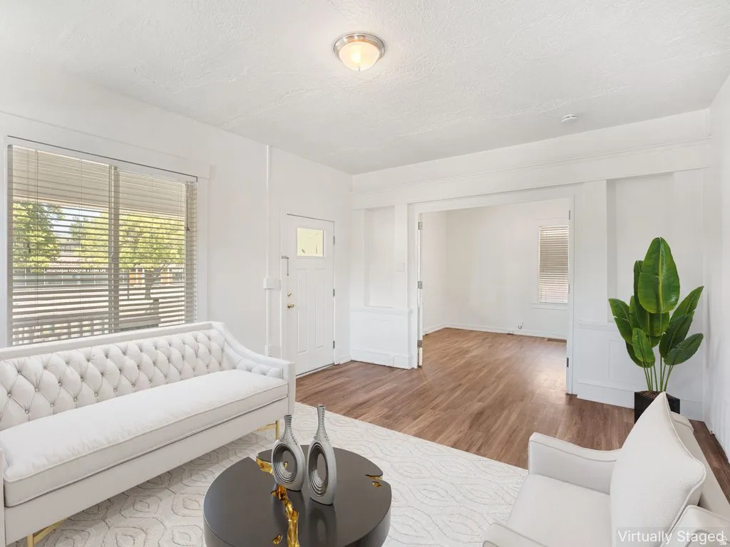 Living area featuring wood-finish flooring, a white paneled entry door with frosted glass, and white window blinds
