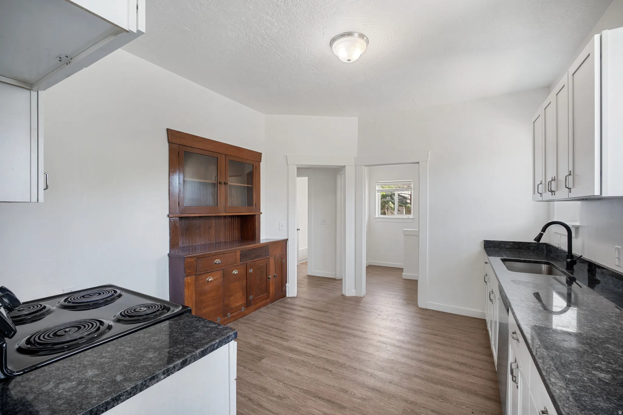 Kitchen featuring wood-finish flooring, white cabinetry, and dark countertops