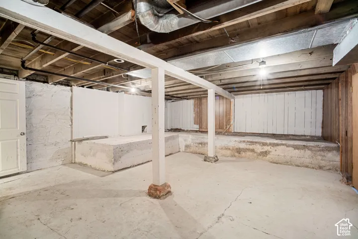 Unfinished basement with concrete flooring and exposed wooden ceiling joists