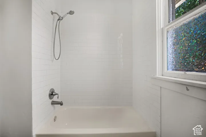 Bathtub with white subway tile surround, polished chrome fixtures, and a decorative privacy window