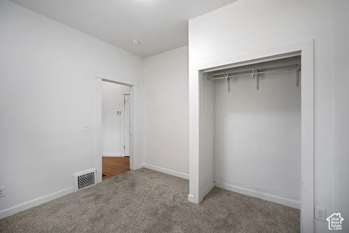 Room featuring light gray carpeting, crisp white walls, a built-in closet with adjustable shelving and hanging rods, and a white baseboard trim