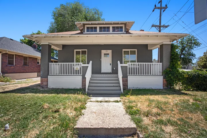Craftsman-style residence featuring a prominent covered front porch with white railing, gray exterior siding, brick foundation accents, and a white entry door