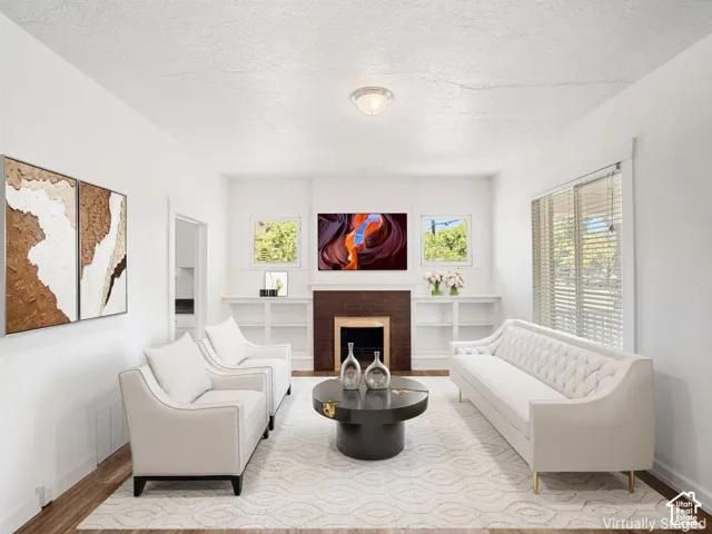 Bright living area featuring wood-finish flooring, a decorative fireplace with a dark wood mantel, built-in shelving, white walls, and a recessed ceiling light fixture