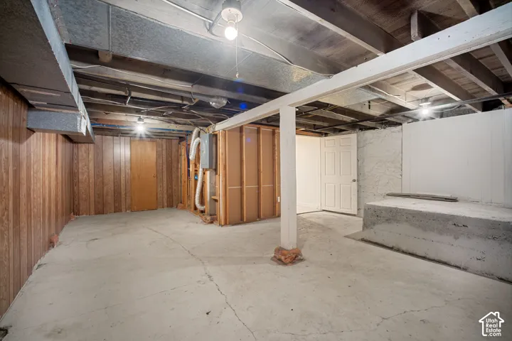 Spacious unfinished lower level featuring exposed ceiling joists, concrete flooring, wood-panel wall accents, and an accessible doorway