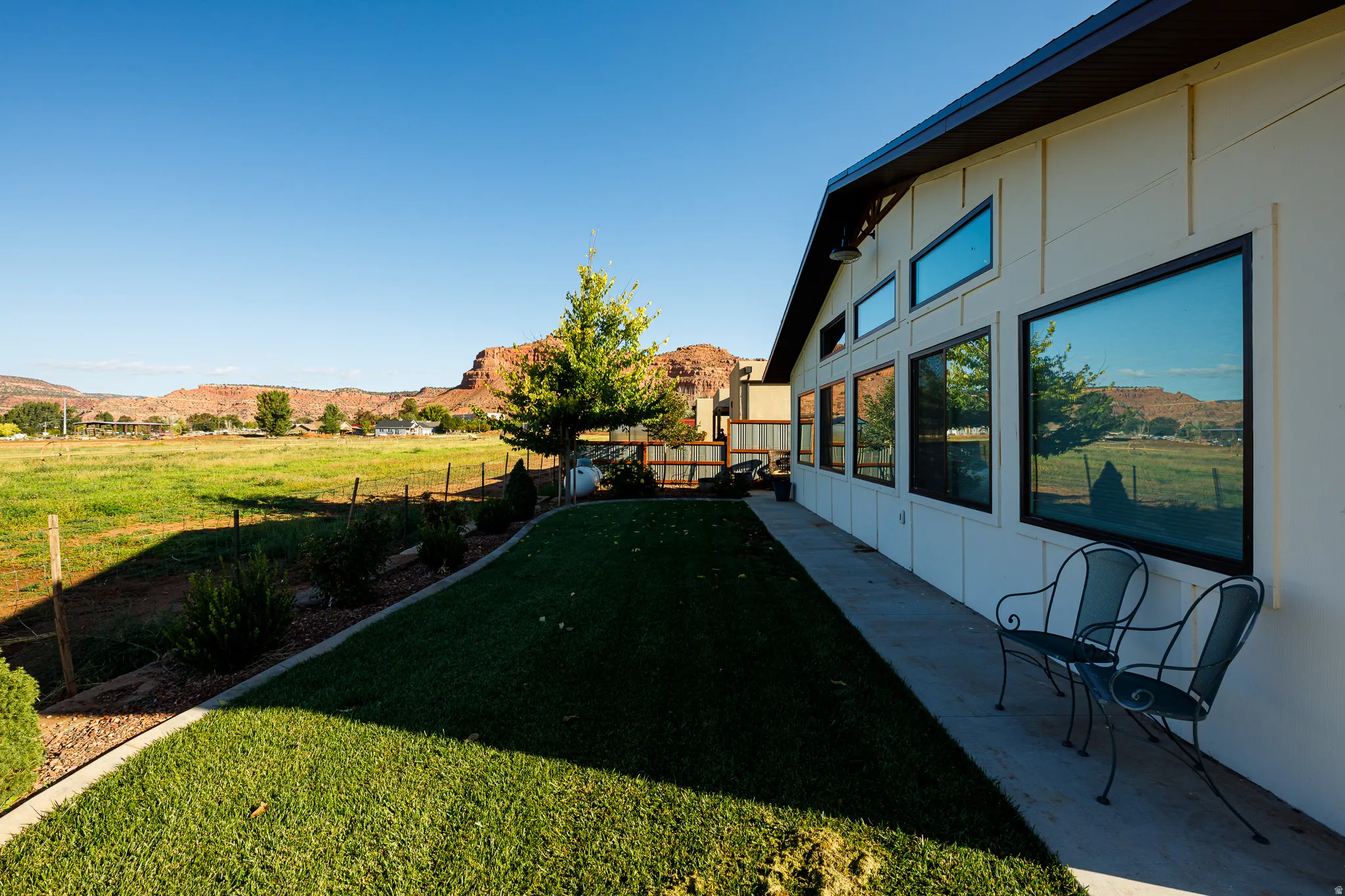 Exterior wall with multiple large windows, a continuous concrete walkway, and a manicured lawn border