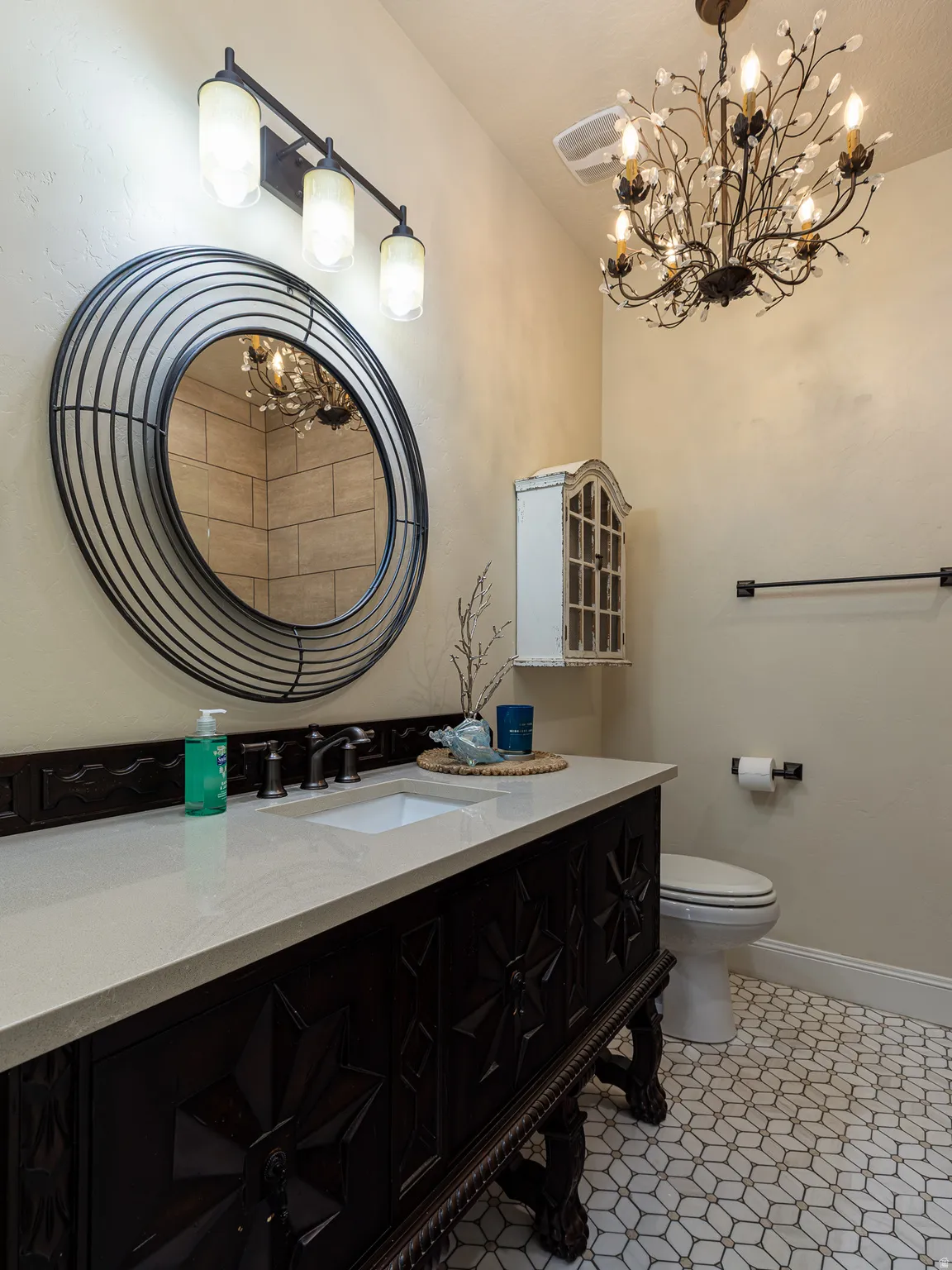 Powder room featuring a dark wood vanity with carved details, a light-toned countertop, a rectangular undermount sink, and a black-framed round mirror