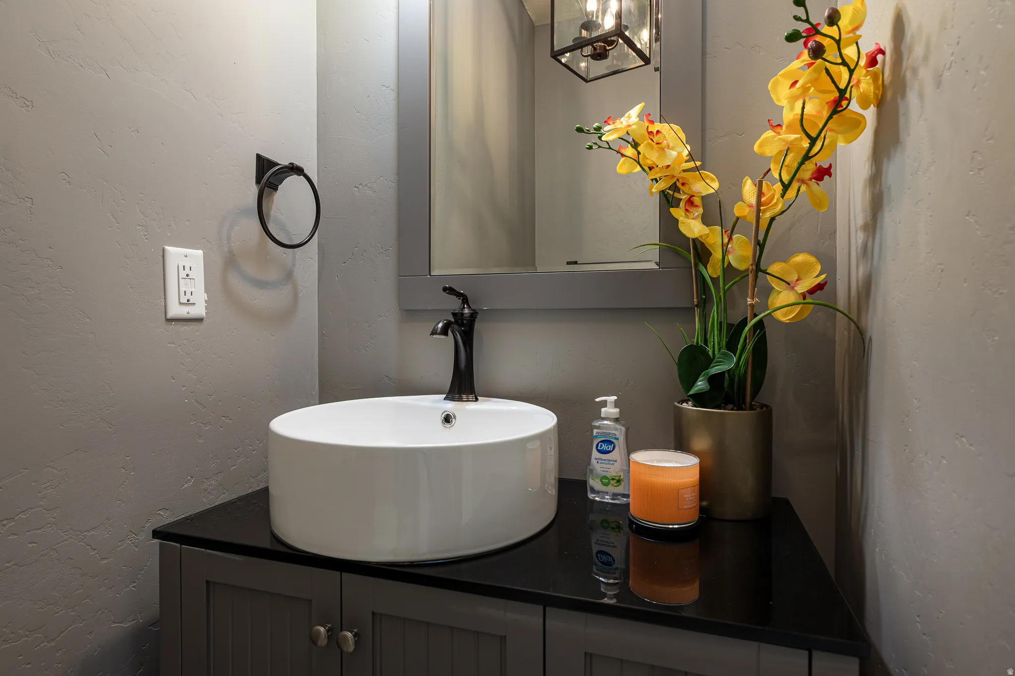 Vanity with a white vessel sink, dark countertop, and dark-bronze faucet