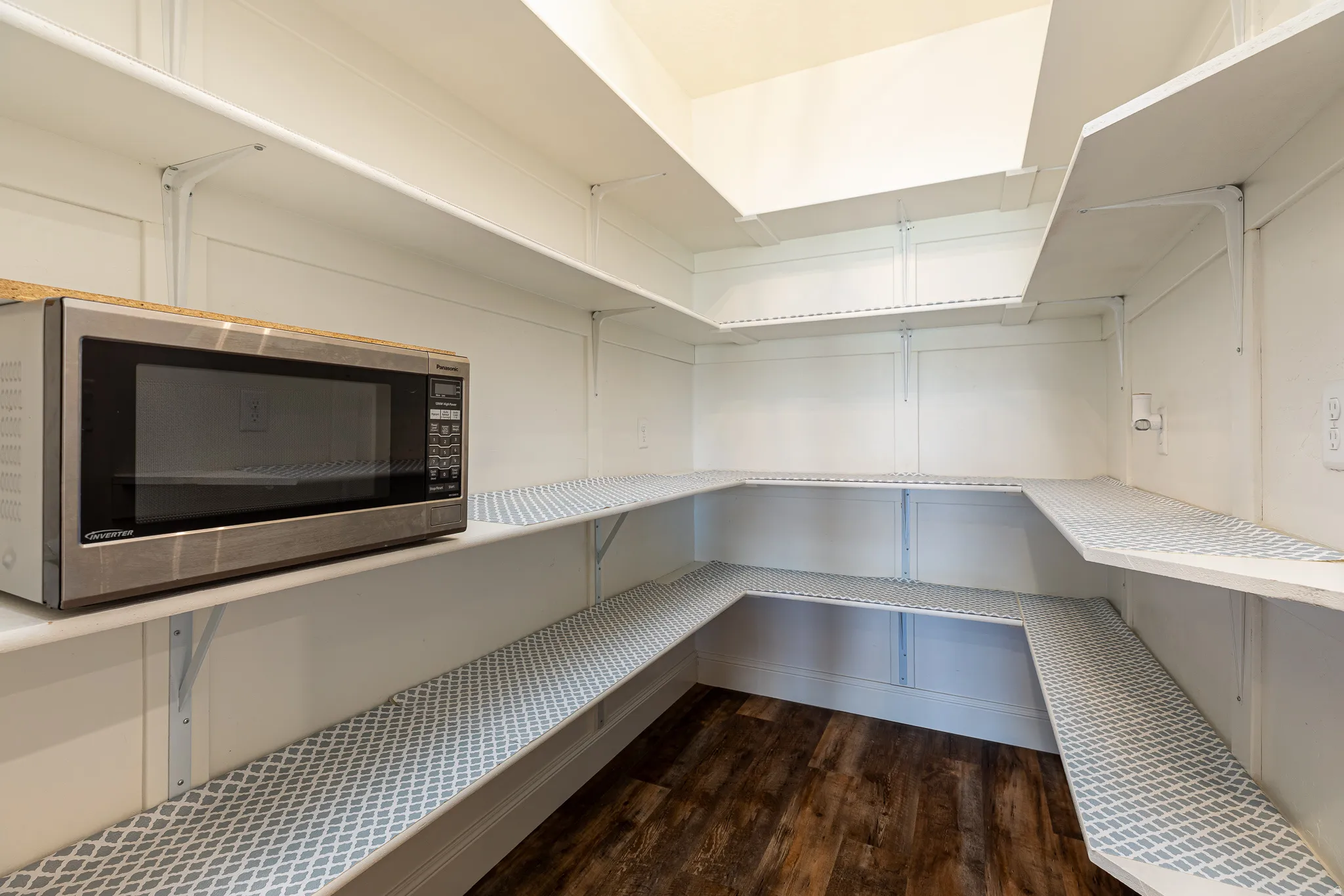 Expansive pantry with multi-level shelving, white wall paneling, and wood-finish flooring