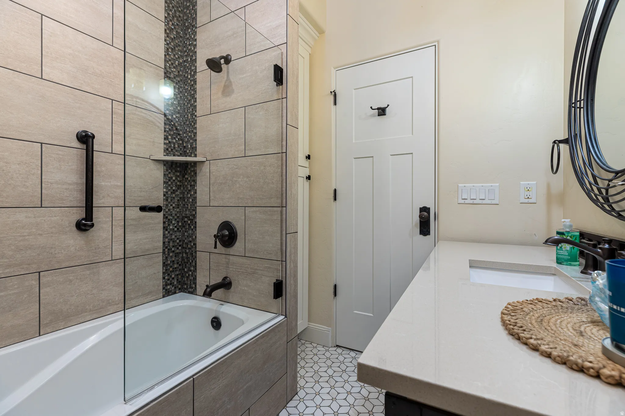Bathroom featuring a bathtub with glass enclosure, beige rectangular wall tiles, and a mosaic tile accent strip