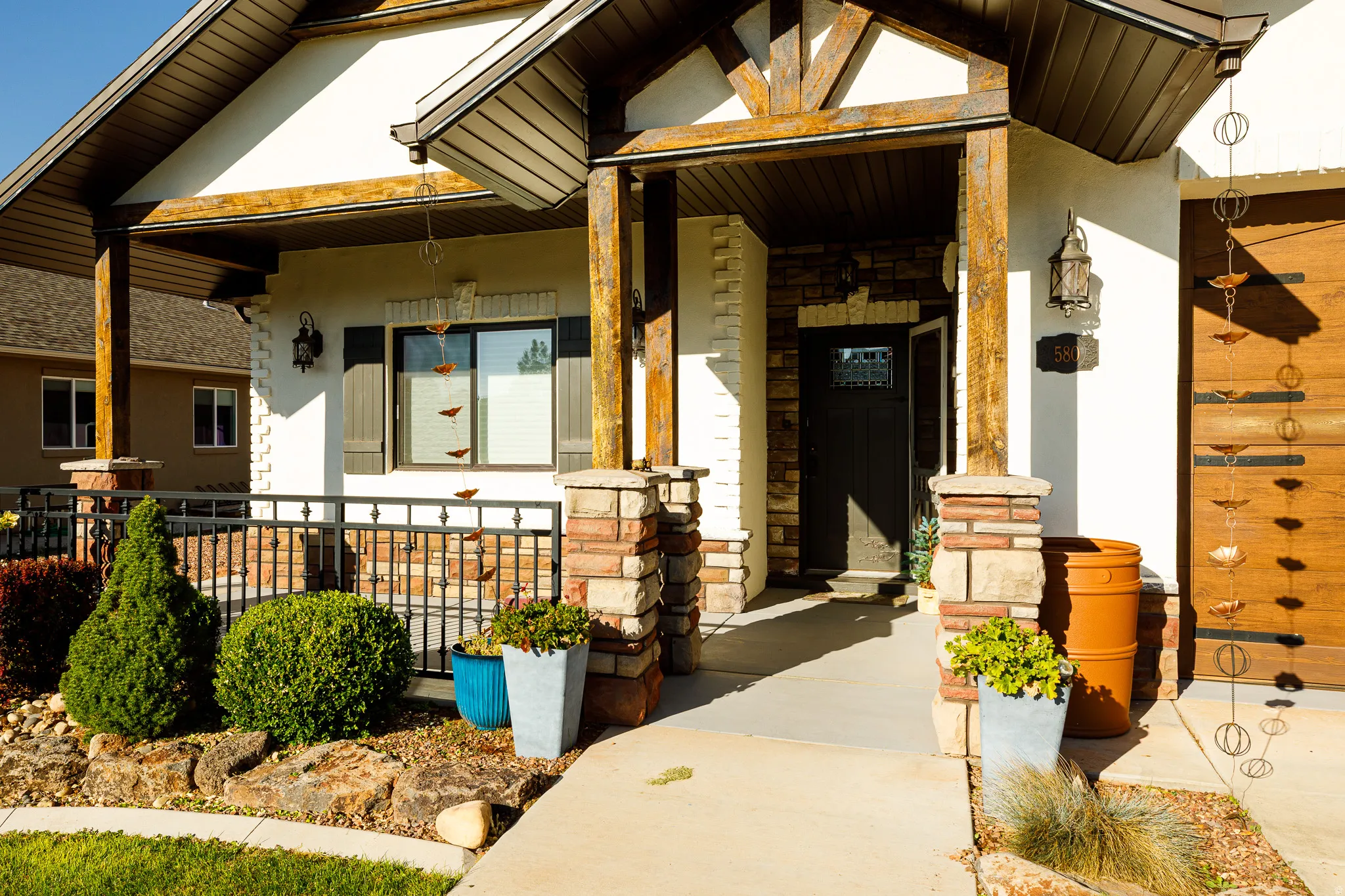 Inviting porch entry featuring rustic wood columns and beams, stone veneer accents, stucco siding, a craftsman-style front door with decorative glass, and a wood-panel garage door