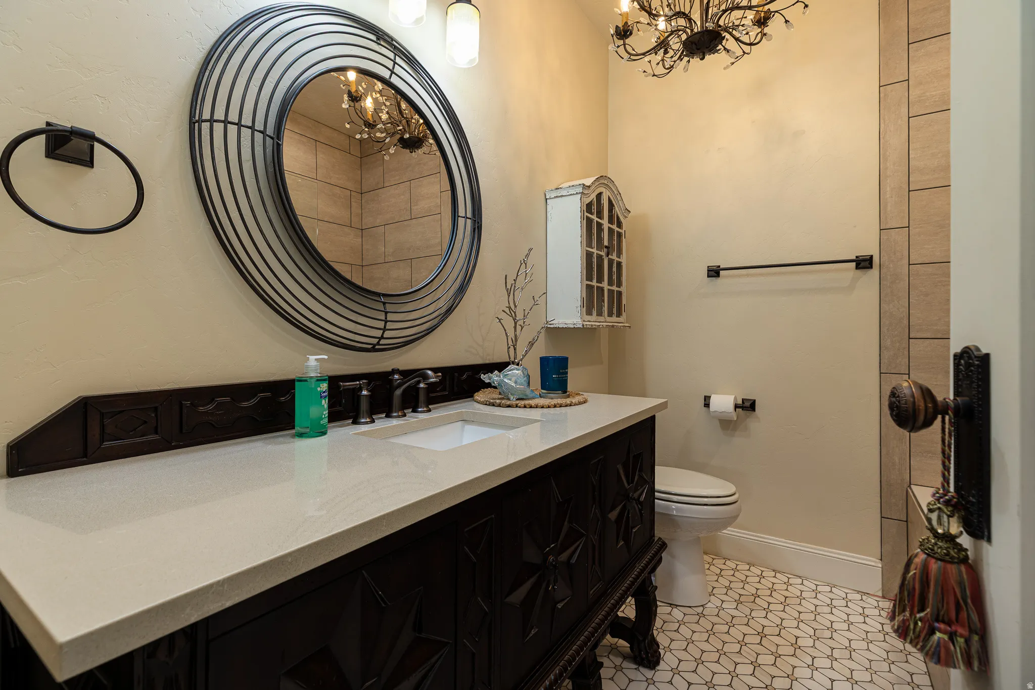 Bathroom featuring a dark wood vanity with a light-toned countertop, a unique circular mirror, and patterned floor tiling