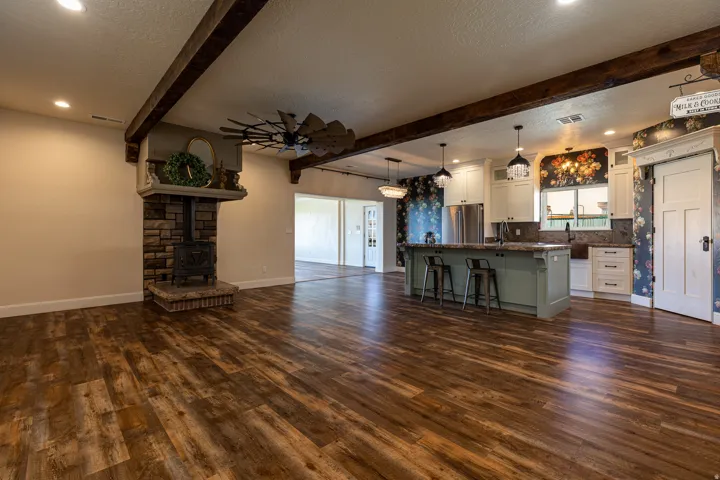 Open-concept living space featuring wood-finish flooring, exposed ceiling beams, and a stone-clad fireplace with an insert