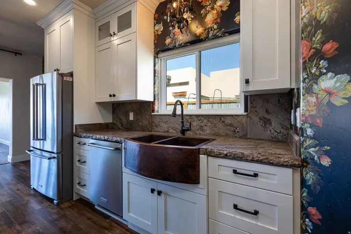 Kitchen featuring white shaker-style cabinetry, a built-in stainless steel refrigerator, a built-in stainless steel dishwasher, a copper farmhouse sink, and stone countertops with a coordinating backsplash